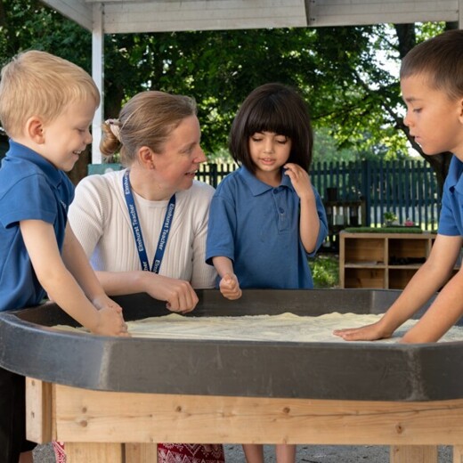 Elmhurst school children playing in sandbox with teacher